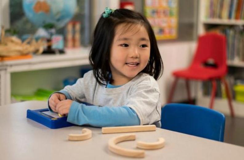 Child using Mat for Wood Pieces to build letters during a hands-on learning activity