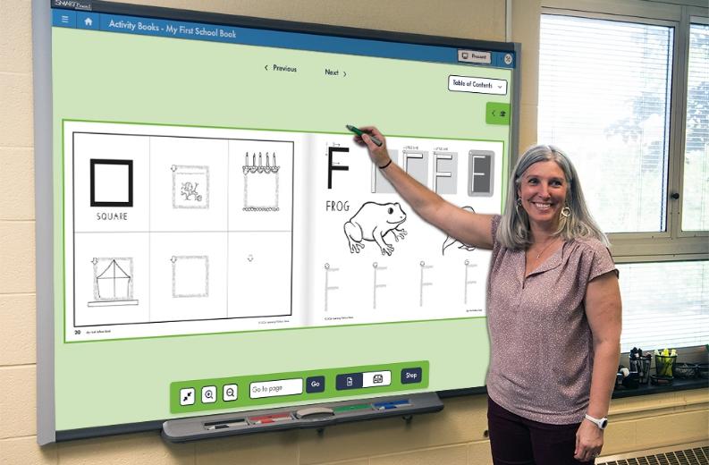 Teacher engaging students by using a digital teaching tool on a tablet or interactive whiteboard during a classroom lesson.